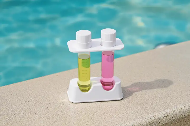 Comparateur d’analyse à deux tubes, l’un jaune, l’autre rose, posé sur la margelle d’une piscine