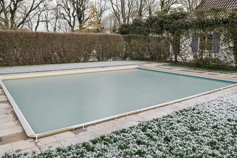 Piscine fermée par une bâche à barres verte en hiver, pelouse couverte de givre au premier plan