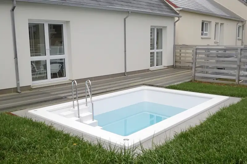 Mini piscine coque blanche de 4 mètres sur 2 enterrée dans la pelouse d’une maison récente