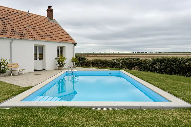 Piscine rectangulaire à escalier d’angle devant une maison basse aux murs blancs, avec les champs plats du marais à l’horizon