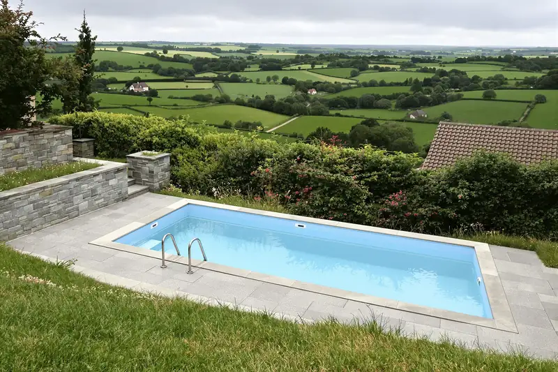 Piscine sur une terrasse en pierre à flanc de coteau, avec vue sur les haies et les prairies du bocage