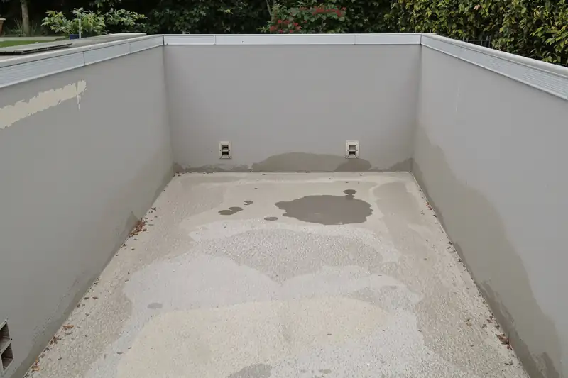 Bassin de piscine vidé, parois grises à l’enduit repris par plaques, fond taché et deux pièces à sceller sur la paroi du fond